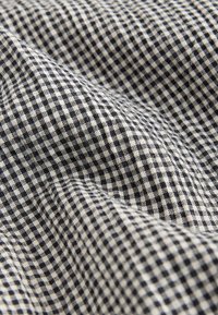 Black and white small checkered fabric with visible texture and stitching, shown in close-up with folds and creases.