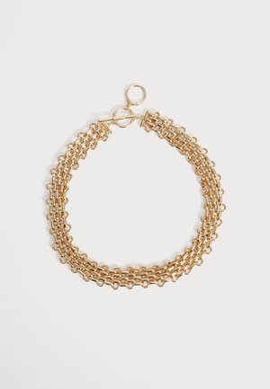 Collier chaîne en or à trois couches avec des maillons circulaires et un fermoir à bascule posé à plat sur un fond clair.