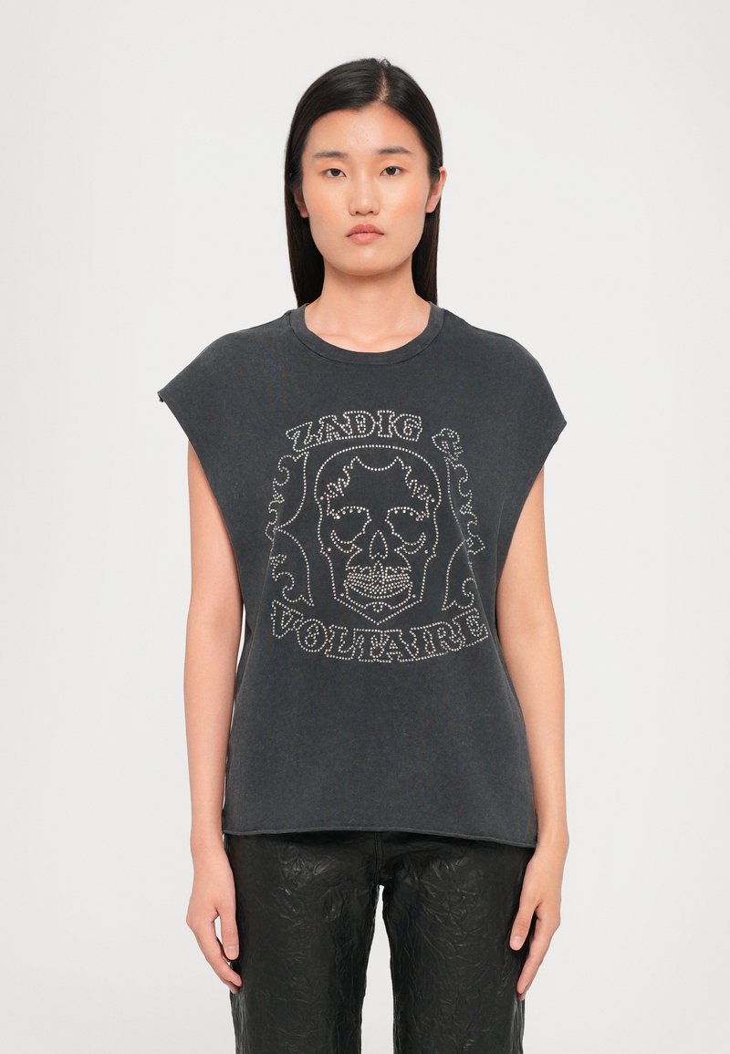 Grijze mouwloze t-shirt met een ronde hals, voorzien van een witte schedelafbeelding en studs met tekstdetails. Draagt met gestructureerde zwarte broek.