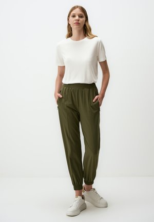 Camicetta bianca a maniche corte e pantaloni elasticizzati verde oliva con bordi, dotati di due tasche laterali e una superficie in tessuto morbida. Sneakers bianche.