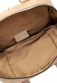 Interno di uno zaino in tessuto beige con una tasca con zip e un ampio scomparto caratterizzato da una consistenza liscia e senza motivi visibili.