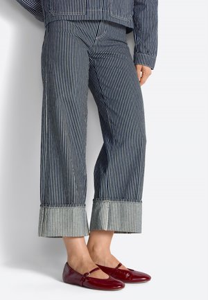 Persona che indossa pantaloni a gamba larga a righe navy e bianche con risvolti e scarpe Mary Jane lucide color bordeaux.