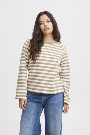 Brown and cream striped long-sleeve top with a round neckline, relaxed fit, and soft texture, paired with blue wide-leg jeans.