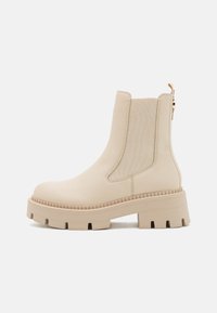 Bottines Chelsea beiges en cuir lisse avec des panneaux élastiques sur les côtés et une semelle en caoutchouc épaisse. Présente des détails cousus et une languette au dos.