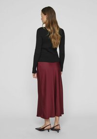 Pull noir à manches longues côtelées associé à une jupe midi satin bordeaux. La jupe a une texture lisse et s'évasent légèrement à l'ourlet.