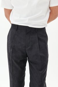 Pantaloni neri a fantasie con vestibilità sartoriale, caratterizzati da pieghe e una texture liscia, abbinati a una camicia bianca semplice.