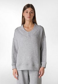 Sudadera gris de gran tamaño, hecha de una tela suave, con un escote redondeado, mangas largas y puños acanalados, con un diseño minimalista.
