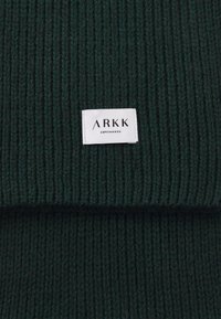 Grøn ribbet strik帽 med et hvidt mærke med "ARKK" og "COPENHAGEN." Teksturen er tykk og hyggelig, velegnet til vinterbrug.