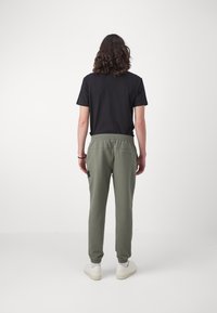 Olivgröna sweatpants med elastisk midja och ankelmanschetter, kombinerade med en svart t-shirt. Vita sneakers kompletterar outfiten.
