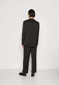 Black tailored suit with a slim-fit silhouette, featuring a notched lapel blazer and straight-leg trousers, made from smooth fabric.