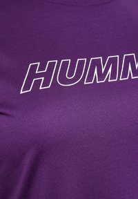 Lila träningsskjorta i strukturerad tyg med en framträdande vit "HUMM"-logotyp på framsidan. Korta ärmar och rund halsringning.