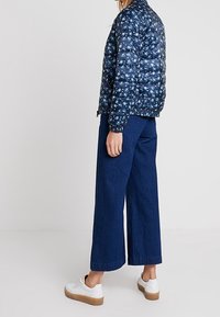 Marineblauwe gebloemde gewatteerde jas met een korte snit, gecombineerd met brede blauwe denimspijkerbroeken en witte sneakers met een tan-zool.