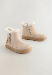 Beige ankelstøvler med faux pelskant, lynlås lukning, dekorative frynser og strukturerede gummisåler. Syet detaljer langs kanterne.