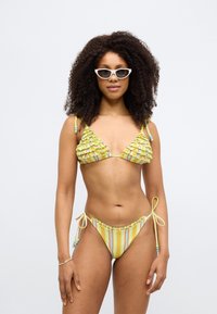 Bikini jaune avec haut triangle à volants et partie inférieure rayée. Liens réglables sur les côtés, perles colorées comme accents, texture lisse.