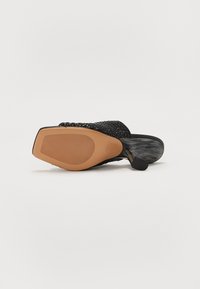 Sandal din material țesut de culoare neagră, cu un superior texturat, o talpă din cauciuc maro și un mic toc. Dispune de un vârf rotund și laterale deschise pentru o mai bună respirabilitate.