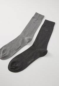 Deux paires de chaussettes : une grise claire et une grise foncée. Chacune possède une texture douce et un logo discret près de la cheville.