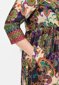 Langärmliges Kleid mit einem mehrfarbigen Paisleymuster auf cremefarbenem Hintergrund, mit umgeschlagenen Manschetten und seitlichen Taschen für zusätzlichen Detail.