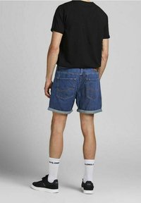 Shorts de denim en azul medio, con dobladillo enrollado y bolsillos traseros. Llevados con una camiseta negra, calcetines blancos y zapatillas negras.