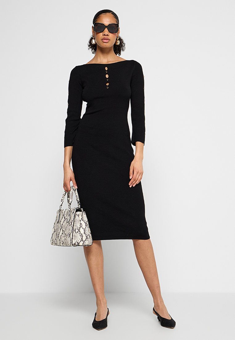 Zwart midi-jurk met driekwartmouwen en een vierkante halslijn, voorzien van drie knopen aan de voorkant. Gecombineerd met een handtas met slangenprint.