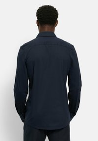 Marineblaues Langarmshirt mit standardmäßigem Kragen, glatter Textur, Knopfmanschetten und abgerundetem Saum. Von hinten vor einem hellen Hintergrund dargestellt.