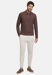 Brauner gestrickter Polopullover, mit Kragen und drei Knöpfen. Kombiniert mit cremefarbenen, schmal geschnittenen Hosen und braunen Wildlederschuhen.