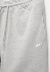 Pantaloni sportivi grigi realizzati in morbido tessuto, con vita elastica e cordino. Presentano un ricamo del logo bianco sul lato inferiore destro.