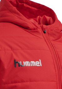 Rode pufferjack met capuchon, voorzien van een ritssluiting aan de voorkant en een glimmend zilveren 'hummel' logo op de linkerkant van de borst. Gestructureerde stof met een doorgestikte ontwerp.