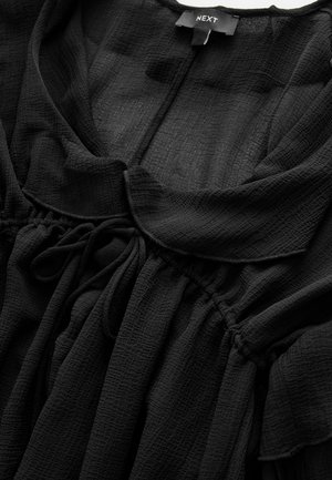 Black, textured blouse with a round collar, gathered waist, and drawstring ties. Made of lightweight fabric, featuring gentle ruffles.