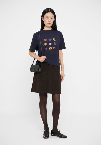 Camiseta de manga corta azul marino con bordado floral. Falda de ante marrón con dos bolsillos frontales. Un bolso negro y zapatos completan el conjunto.