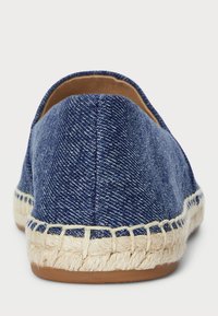 Pantofii slip-on din denim albastru, cu un spate rotund, talpă din jute și detalii cusute de-a lungul marginii. Căptușeala moale vizibilă la deschidere.