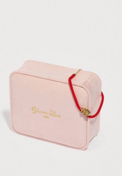 Ροζ ορθογώνιο σουέντ τσάντα με χρυσό λογότυπο, κόκκινη λαβή από σκοινί και χρυσή λεπτομέρεια, με στρογγυλεμένες γωνίες και μαλακή υφή.