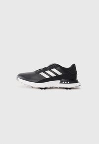 Black athletic shoe with white stripes, textured upper, round toe, and a white rubber outsole featuring small spikes for traction.