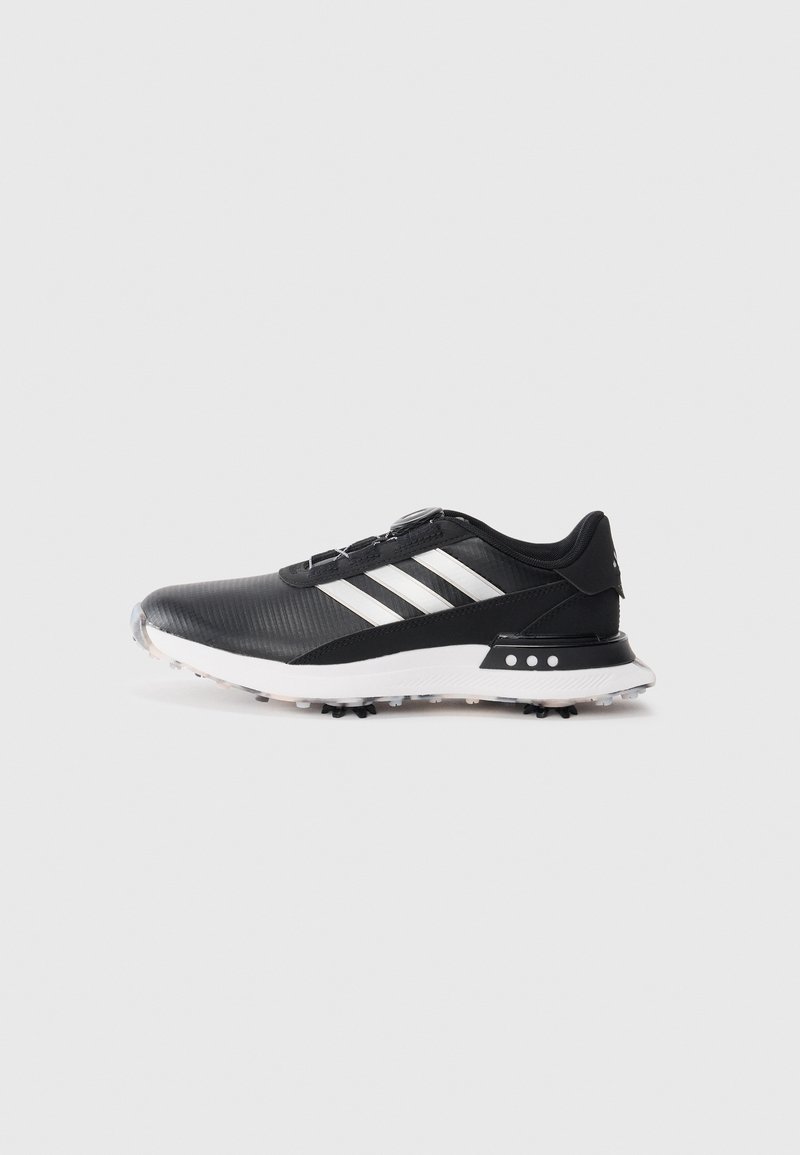 Black athletic shoe with white stripes, textured upper, round toe, and a white rubber outsole featuring small spikes for traction.