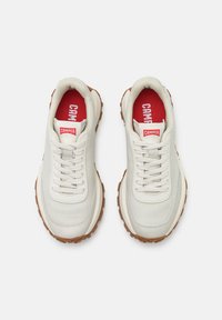 White leather sneakers with a padded tongue, round laces, red inner lining, and rubber outsole featuring textured brown accents.