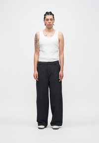 Balts tanktkrekls, melnas platām biksēm un balti sporta apavi; gluda auduma tekstūra; vienkāršs dizains ar piegriezumu un priekšējām kabatām.