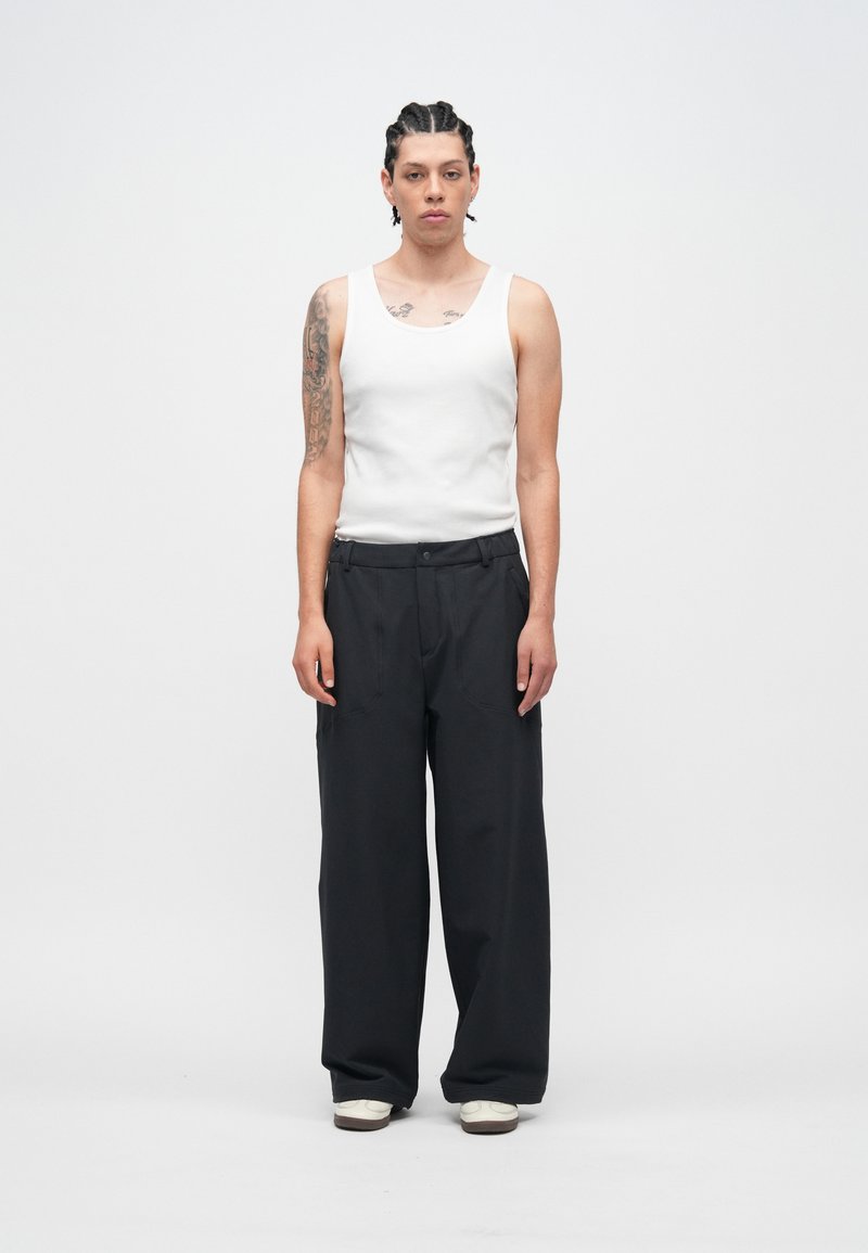 Balts tanktkrekls, melnas platām biksēm un balti sporta apavi; gluda auduma tekstūra; vienkāršs dizains ar piegriezumu un priekšējām kabatām.