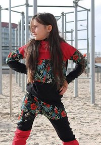 Kolorowy komplet odzieży sportowej z kwiatowym wzorem w odcieniach zieleni, czerwieni i czerni. Posiada wysoki kołnierz i długie rękawy, o luźnym kroju.