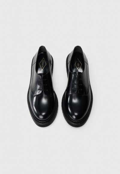 Pantofi derby din piele neagră cu finisaj neted, vârf rotund și sistem de închidere cu șireturi. Prezintă o talpă groasă din cauciuc cu un model texturat.