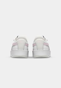 Zapatillas blancas con acentos rosas, materiales de cuero liso y textil, forma redondeada y suelas de goma. Presenta el logo de Puma en el talón.