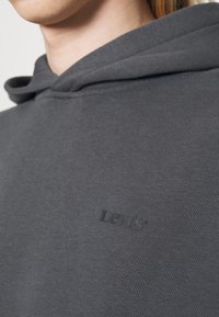 Felpa grigia realizzata in morbido tessuto, con cappuccio regolabile tramite coulisse e un sottile logo impresso di Levi's sul petto.