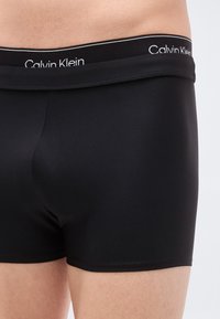 Μαύρα μπόξερ σορτς από βαμβακερό μείγμα με εφαρμοστή γραμμή, με ζώνη μέσης που φέρει το λογότυπο "Calvin Klein" σε λευκό. Ομαλή υφή και μινιμαλιστικός σχεδιασμός.