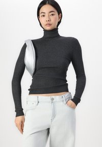 Grå ribbet høyhalset genser med lange ermer, sammen med lys blå høyt midje jeans, med et sølvtilbehør over skulderen.
