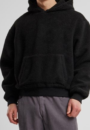 Sudadera con capucha negra hecha de un suave forro polar texturizado, con un bolsillo frontal y puños y dobladillo acanalados, combinada con pantalones claros a rayas.