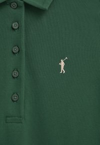 Polo vert foncé avec quatre boutons et joueur de golf beige brodé portant un club sur le côté gauche de la poitrine.