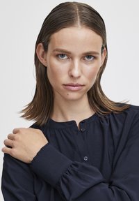 Marineblauwe button-up shirt met een ronde hals en gerimpelde manchetten. Glad stof met een subtiele glans en een ontspannen pasvorm.