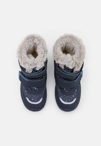 Botas para niños de color azul marino con forro de piel sintética gris oscuro, dos correas ajustables de Velcro y un patrón de lunares en material sintético.