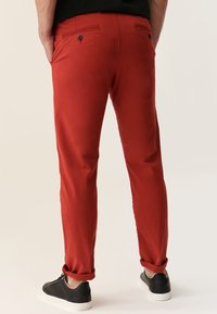 Pantalones de algodón rojos con un corte slim, que presentan dos bolsillos traseros con botones, puños remangados y combinados con zapatillas negras.