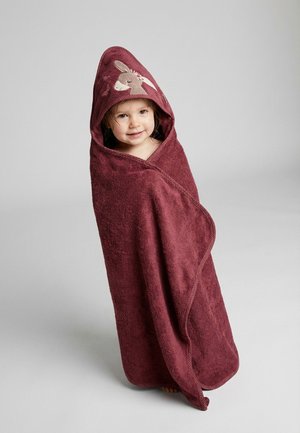 Toddler wrapped in a maroon hooded towel with a donkey design on the hood, standing against a plain light gray background.