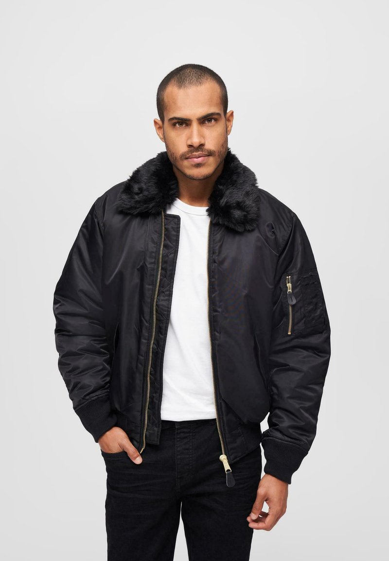 Chaqueta bomber negra con cuello de piel sintética, cierre de cremallera al frente y bolsillos laterales. Presenta una textura suave y puños acanalados.