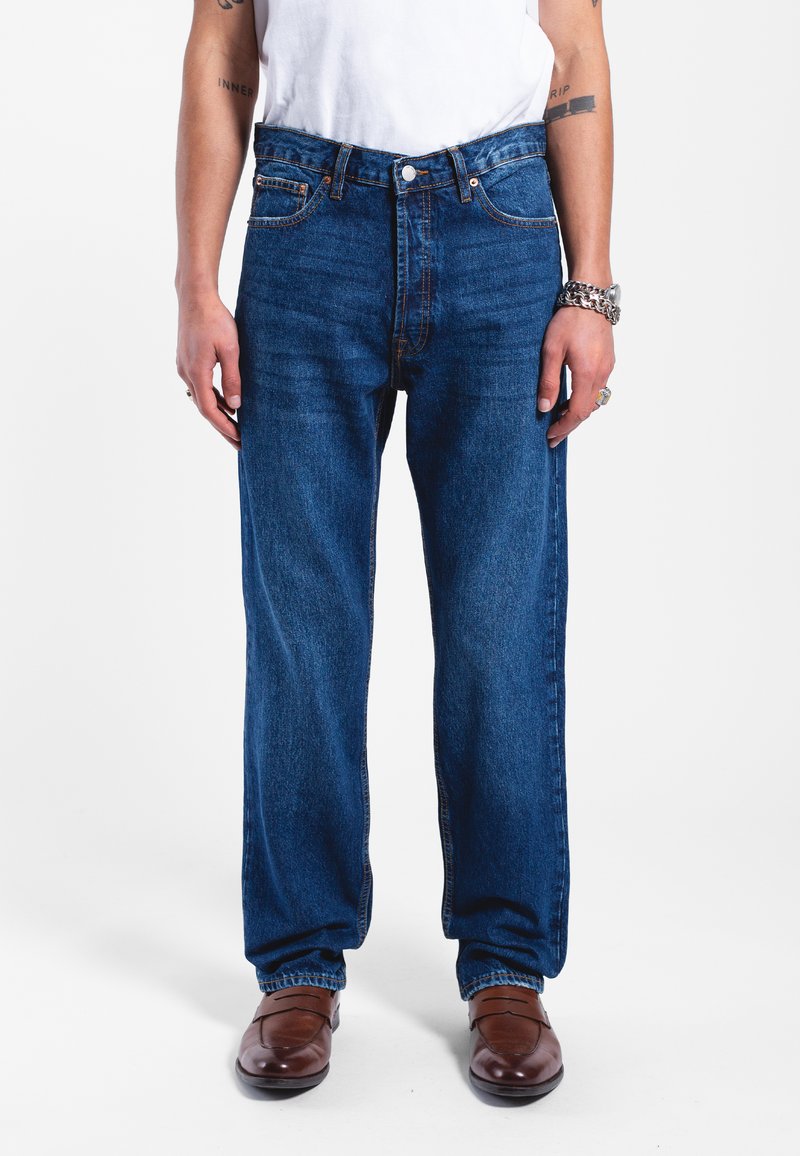 Jeans de mezclilla azul con un corte relajado, pierna recta y un diseño clásico de cinco bolsillos. Presenta remaches de cobre y sutiles acentos de costura.